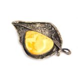 An amber brooch, formed as a leaf with rough detailing and applied butterscotch amber bead, in a whi