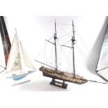 A painted model of a ship, with realistic rigging and deck, and a further painted yacht on wooden st