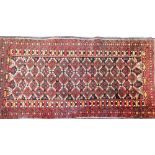 A Baluch red ground rug, decorated with repeated medallions, within floral and geometric borders, 20