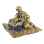 A 20thC cold cast bronze figure, of an Arabian gentleman seated on a carpet reading, in the manner o