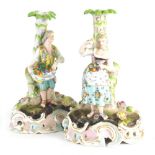 A pair of Meissen style porcelain candlestick groups, formed as a lady and gentlemen, each dressed i