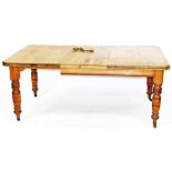 A Victorian pine wind out dining table, with one additional leaf, raised on turned legs, brass cappe