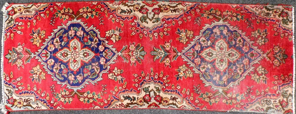 A Keshan red ground runner, with two central blue medallions decorated with flowers, against a flora