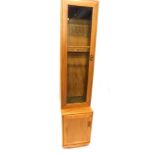 An Ercol light elm narrow cabinet, the top with a single glazed door with bevelled glass, the base w