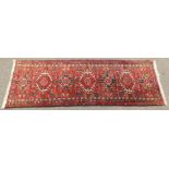 A Persian rug, with six central medallions on a red ground with multi coloured border, 196cm x 68cm.