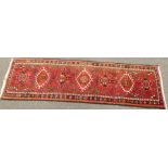 A Persian runner, with six central medallions on a red multi coloured ground, 196cm x 63cm.
