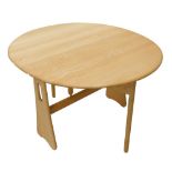 An Ercol light elm drop leaf table, the oval top with a shaped edge on pierced end supports, 107cm w