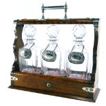 A 20thC oak Tantalus, with chrome plated mounts and three cut glass decanters, each with spirit labe