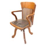 An early 20thC oak office chair, with a slatted back and a padded seat, on four splayed legs.
