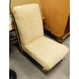 A nursing chair, overstuffed in straw coloured material on turned front legs, terminating in castors