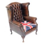 A brown leather wing back chair, with button back and union jack covered seat, raised on cabriole le