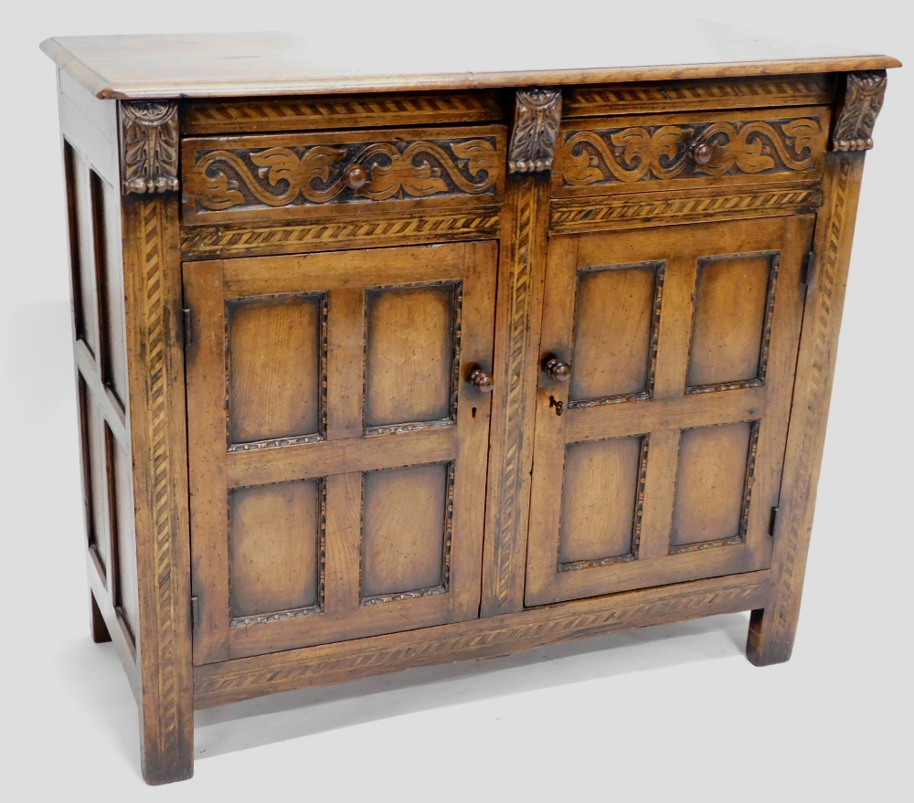 An oak side cabinet, the rectangular top with two carved frieze drawers and two panelled doors on st