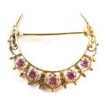 A crescent moon brooch, set with five rubies in claw setting with filigree type detail, yellow metal