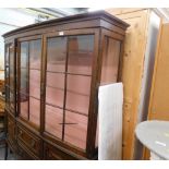 An Edwardian mahogany display cabinet, with glazed panel flanked by doors, raised above two central