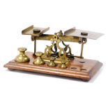 A set of early 20thC brass postal scales, with weights, on a wooden base, 24cm wide.