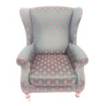 A Parker Knoll wingback armchair, upholstered in green patterned fabric on turned legs.