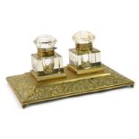 A continental brass desk stand, the central rectangular panel, with two cut glass inkwells, with scr