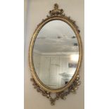 An early 19thC oval giltwood wall mirror, with Neo Classical urn and bell husk decoration, 97cm high