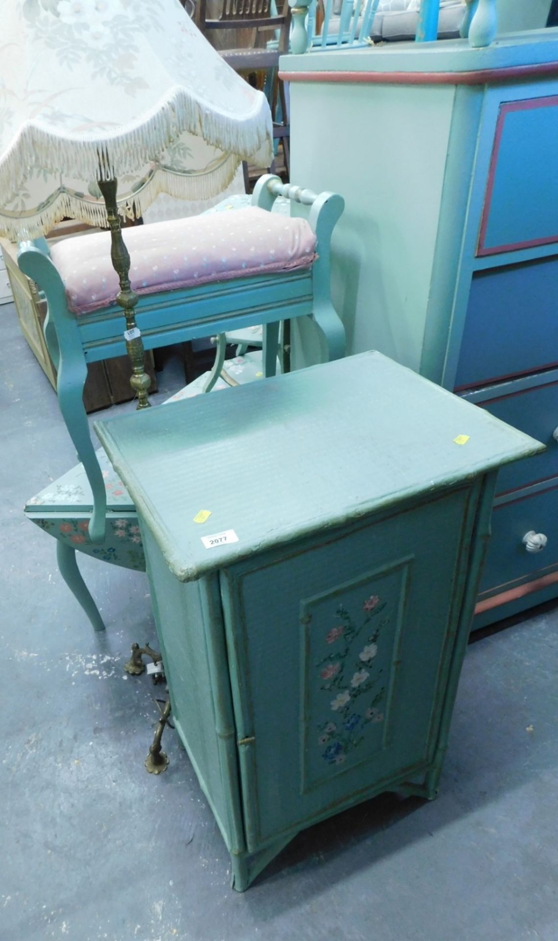 A painted bamboo finish side cabinet, decorated with flowers and a standard lamp.