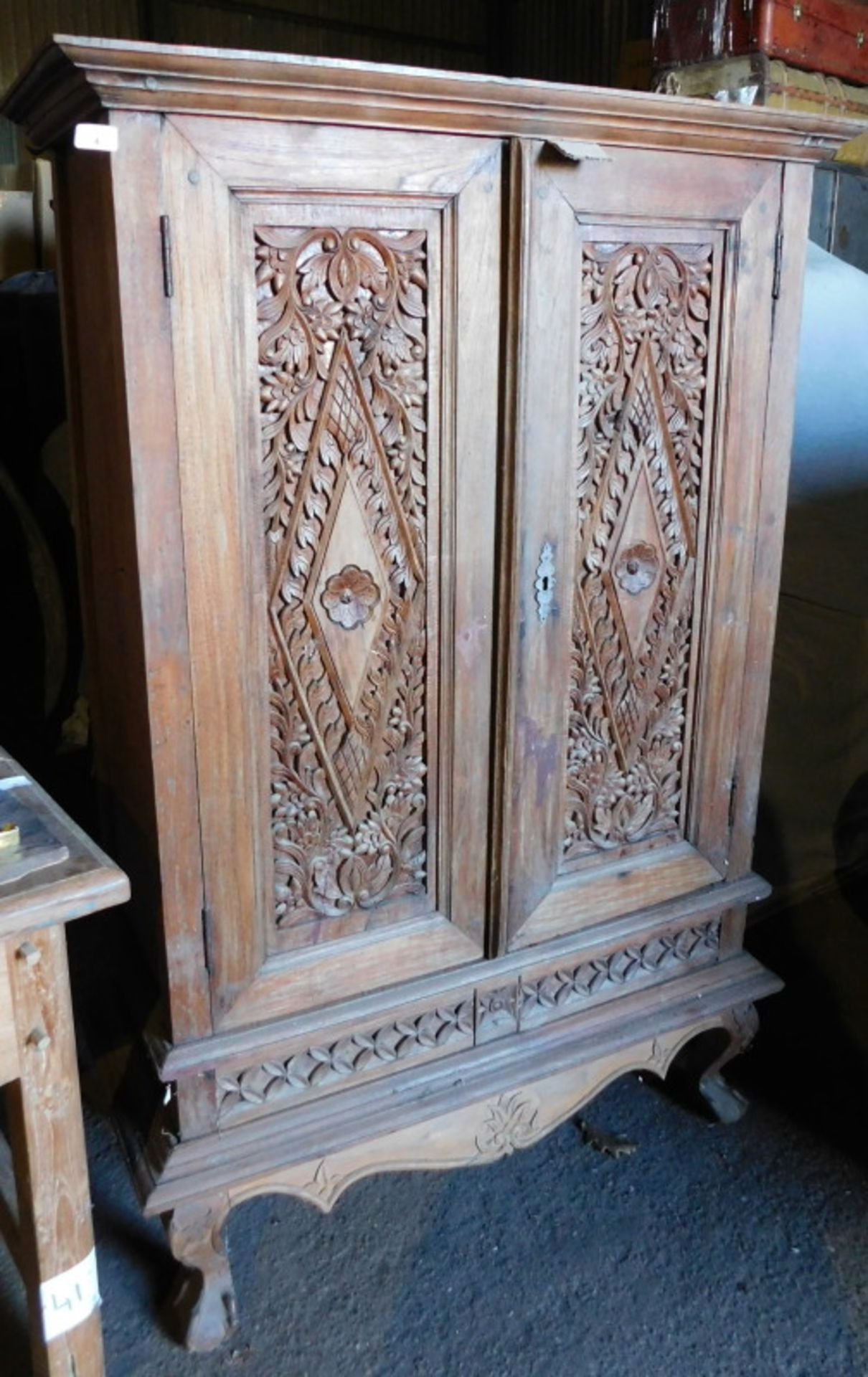 An Eastern teak cabinet, the top with a moulded cornice above two carved panelled doors, above a sha