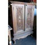 An Eastern teak cabinet, the top with a moulded cornice above two carved panelled doors, above a sha