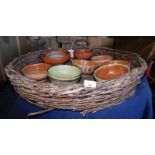 A wicker basket, of circular form with handles, containing a quantity of terracotta bowls, some pain