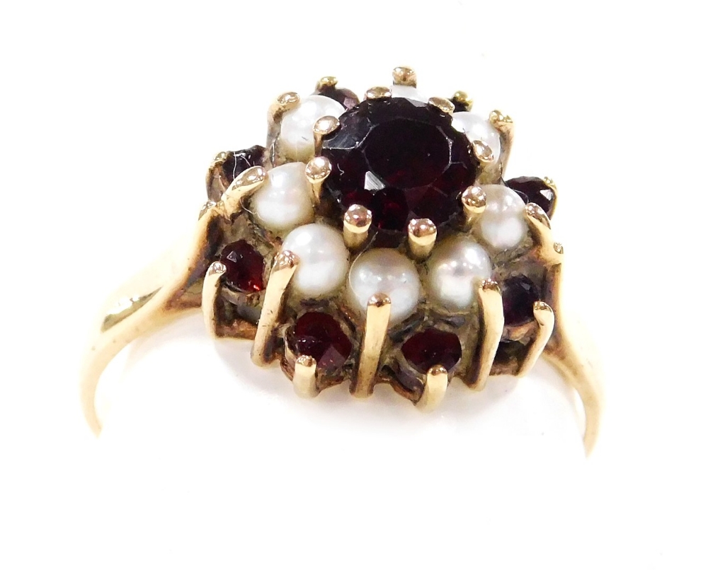 A 9ct gold garnet and seed pearl ring, of concentric flower head form, high claw set, size O, 3.0g.