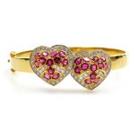 A ruby and diamond set hinged bangle, with two heart shaped motif to the front, each set with twelve