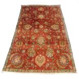 A Sarouk red ground rug, decorated with bold floral motifs, within a repeating floral border, 277cm