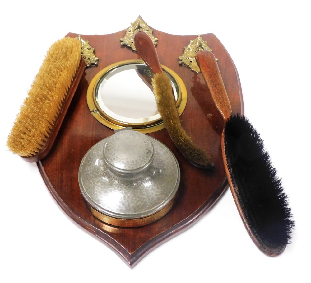 An early 20thC shield shaped hall wall mirror, inset bevelled glass, below three brass hooks holding