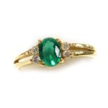 An emerald and diamond set dress ring, the oval faceted emerald of 5.2mm x 4mm with two tiny diamond