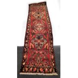 A Hamadan red ground runner, decorated with three central floral medallions, further flowers and lea