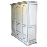 A cream and pale blue painted pine triple wardrobe, the outswept pediment over three doors, enclosin