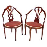 A pair of Edwardian mahogany armchairs, each with carved splats, oval red draylon seats, raised on c