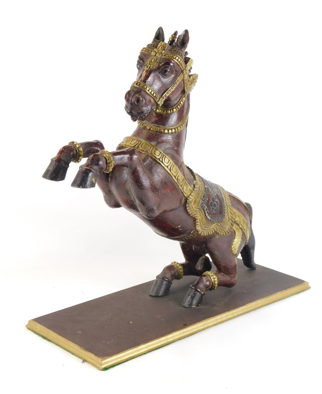 An Eastern hardwood carving of a rearing horse, on a red lacquer painted ground, with gold painted b