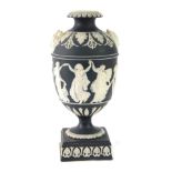 A Wedgwood black basalt urn, on black ground with white dancing figures on a stepped foot lacking co