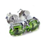 A pair of peridot stud earrings, each with an oval peridot, in a four claw basket setting, on single