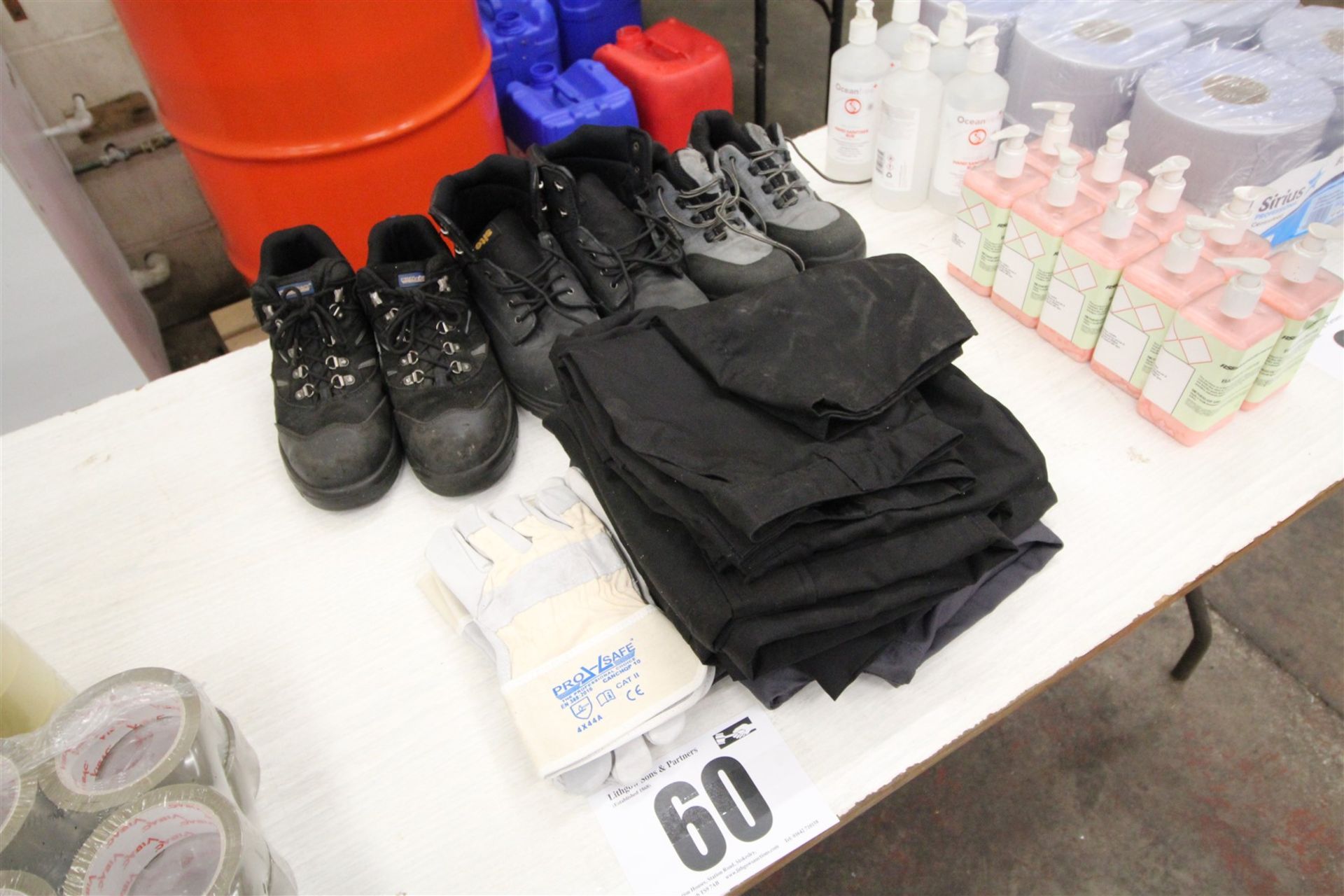 Contents on Middle of Table of 3x Pairs of Safety Boots, 4x Pairs of Trousers, and 3x Pairs of