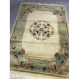 Cream ground woollen rug with green border ad pink/blue design, approx 200cm x 135cm