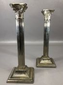 Pair of silver coloured Corinthian column candlesticks on square stepped bases, stamped 'Made in