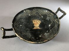 Greek pottery Kylix with remains of black glaze bearing figure of a man's head, twin handles,
