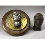 Two male heads, one carved from wood, the other moulded out of metal and mounted on a circular brass