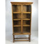 Glass fronted two door bookshelf / display cabinet raised on turned legs, approx 91cm x 30cm x 187cm
