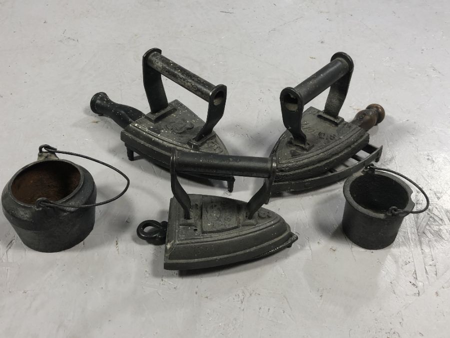 Collection of flat irons and two small cast iron pots