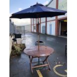 Circular teak garden table and parasol with wrought iron base, table approx 120cm in diameter