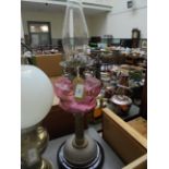 Paraffin lamp with cranberry glass bowl supported by brass corinthian column on circular black pot