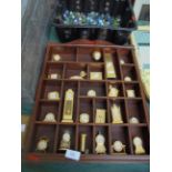 Collection of 24 miniature brass clocks as displayed within the wooden wall case
