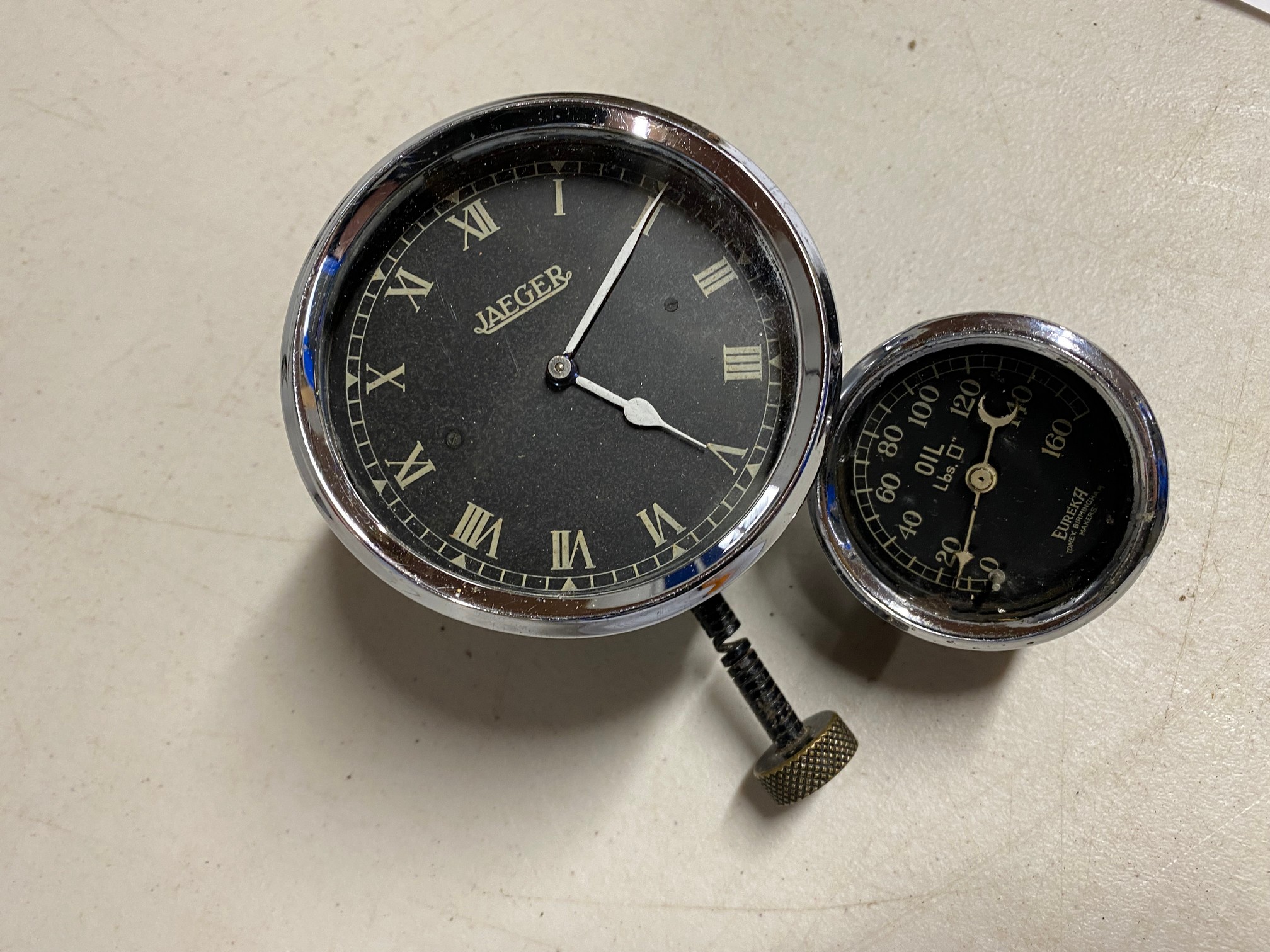 A Jaeger black faced bottom wind car clock plus a Eureka oil pressure gauge.