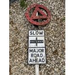 A metal road sign mounted on a tall post, surmounted by a warning triangle in a circle with integral