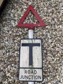 A metal road sign for Road Junction mounted on a tall post, surmounted by a warning triangle.